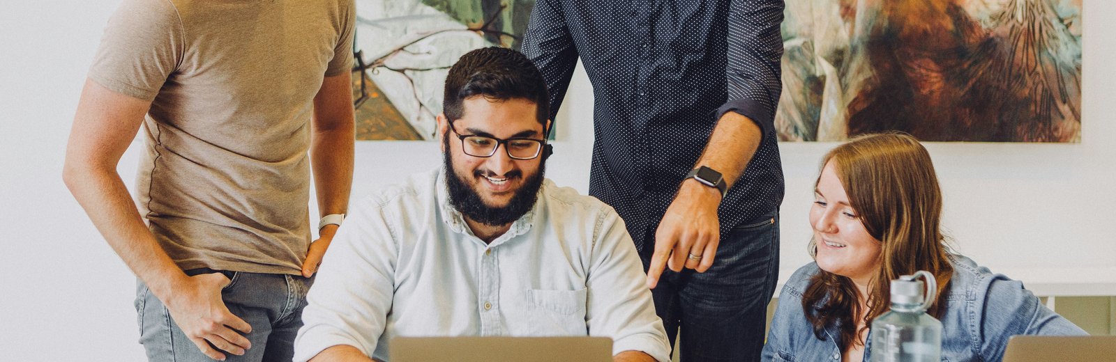 Four colleagues smiling and collaborating around a laptop during a meeting