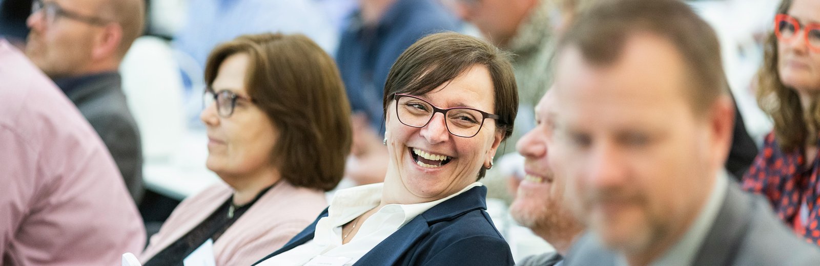 A group of professionals attending a workshop, smiling and interacting with handheld devices, representing active learning and engagement.