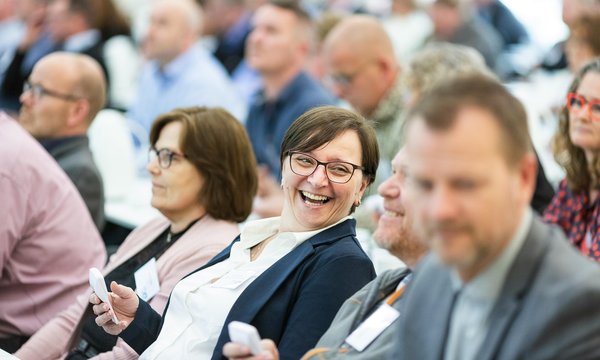 A group of professionals attending a workshop, smiling and interacting with handheld devices, representing active learning and engagement.