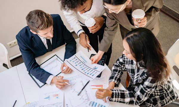 Business professionals gathered around a table reviewing charts and graphs during a consulting session.